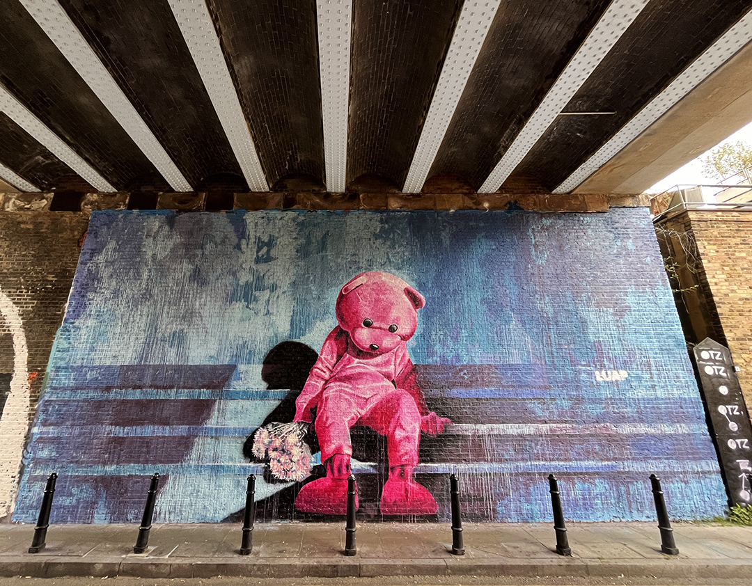 stunningly melancholy pink bear sitting on a bench by street artist Luap